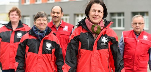 Fünf Menschen mit caritas-roten Jacken an