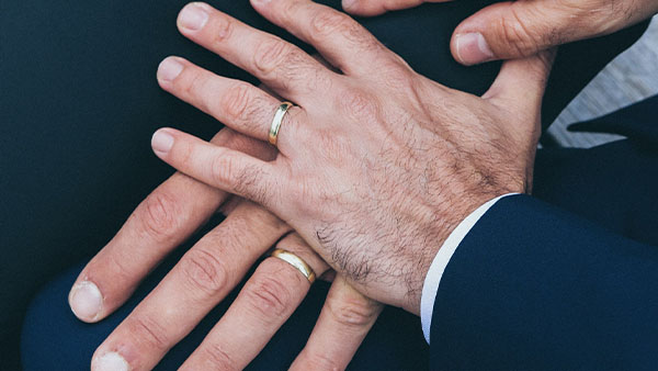 Zwei männliche Hände mit Eheringen liegen übereinander.