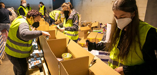Mehrere Menschen in gelben Warnwesten packen Lebensmittel in Kartons.