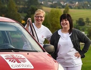 Caritas-Mitarbeitende vor einem roten Caritas-Auto