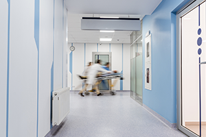Aufnahme Krankenhausflur mit drei im schnellen Tempo davoneilenden Personen mit Krankenbett