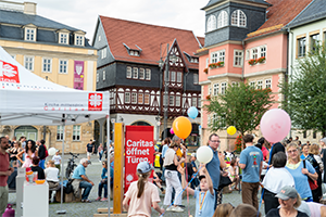 Zahlreiche Menschen stehen lose auf einem Platz mit mittelalterlichen Häusern