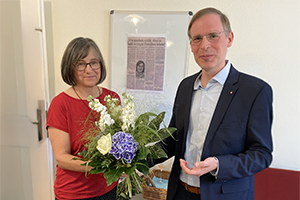 Mann und Frau lächeln in die Kamera und halten dabei beide an einem Blumenstrauß