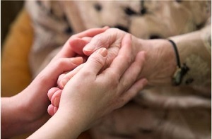 Hände eines älteren Menschen werden von denen einer jungen Frau umfasst.