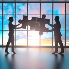 Silhouetten von Personen, die gemeinsam ein Puzzleteil zusammensetzen
