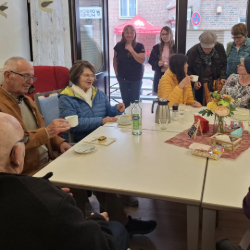 Menschen sitzen um einen Tisch, trinken Kaffee und essen Kuchen