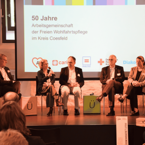 F&uuml;nf Personen sitzen auf einer B&uuml;hne
